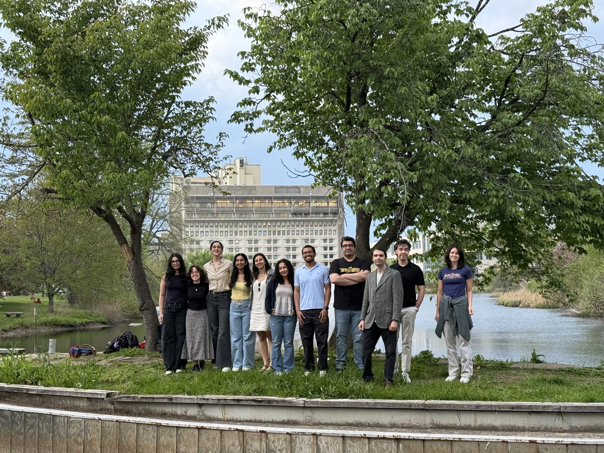 Lab members gathered by the campus pond, with the library tower behind.